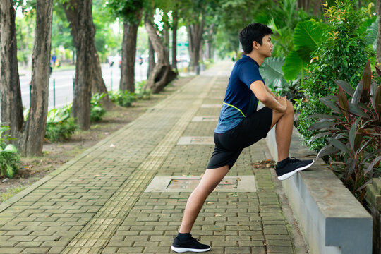asian young fitness man runner do a strething leg before running at the park
