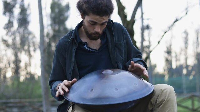 Concentrated musician playing handpan in an outdoor park. Alternative style.