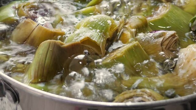 Boiling artichokes in saucepan, closeup in kitchen