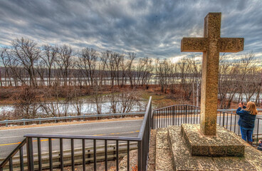 Obraz premium picture taken from Pere Marquette Cross looking out over the Illinois river in winter, cloudy sky with sunlight breaking through in places, unknown photagrapher taking a photo beside cross 