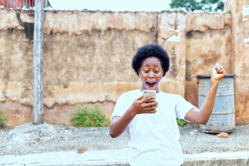 image of a pretty african girl holding a mobile phone with a surprise, happy and joyous face.