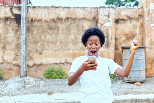 image of a pretty african girl holding a mobile phone with a surprise, happy and joyous face.