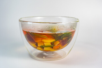 Vegetables soup in double-walled glass bowl on white background