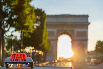 Parisian taxi roof sign in front of the Arc de Triomphe in Paris under a sunset. 