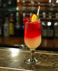 Cocktail drinks. A glass of red cocktail with cherries, set against a bottle of alcoholic drinks at the bar.