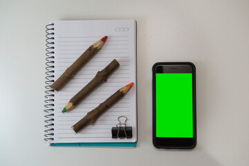 Top view of office desk with blank note book, rustic colored pencils and smartphone.