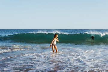 Young girl in ocean water looking back at approaching wave. Summer fun on a beach.