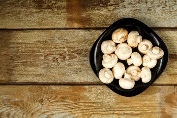 Champignons in a black plate on a table of rough boards.