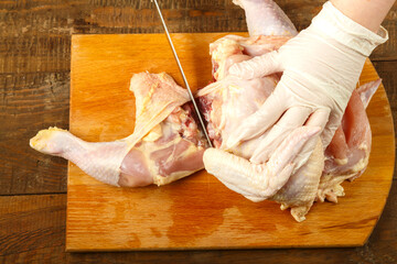 A female hand in gloves cuts off chicken pieces with a sharp knife. © finist_4