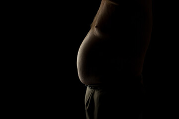 A fat man with a big belly backlit on black background