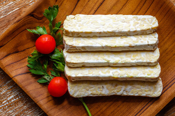 Raw tempeh (traditional Indonesian soy product), cherry tomatoes and parsley on wooden surface. Top view. 