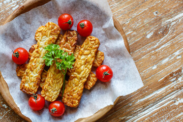 Fried tempeh or tempe (traditional Indonesian soy product), cherry tomatoes and parsley on wooden surface. Top view. With space.