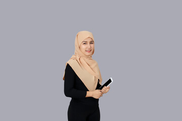 Happy asian muslim woman smiling wearing hijab head scarf and holding tablet over gray background.