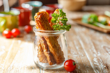 Fried tempeh or tempe (traditional Indonesian soy product) in a small glass jar on wooden surface. Side view. With space.