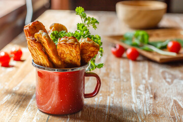 Red enameled cup with fried tempeh or tempe (traditional Indonesian soy product) on wooden surface. Side view. With space.