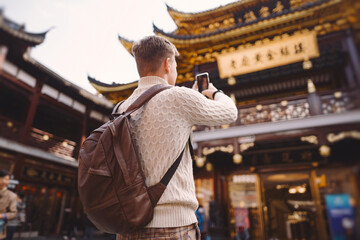 male tourist taking photos of a pagoda at Yuyuan market in Shanghai during his visit to China