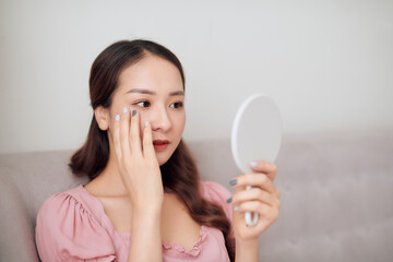 Beautiful face young Asian woman looking at the mirror, with cosmetic treatment, healthy concept.