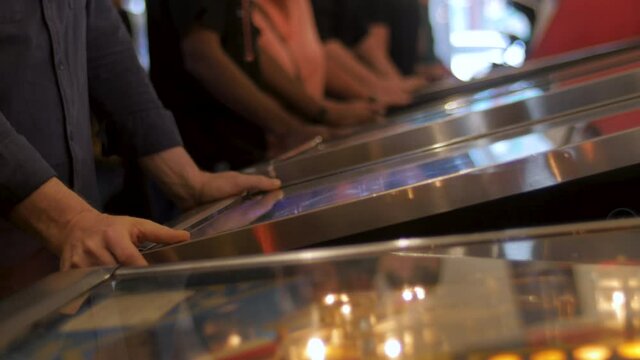 Man playing at a pinball table in a busy arcade