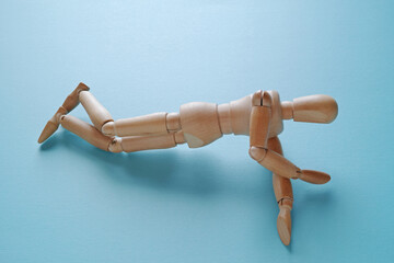 青背景で回復体位のようなポーズの木製のモデル人形【正面　右向き】