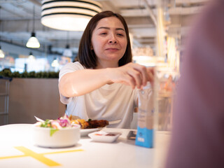 Asian woman sitting separated in restaurant eating food with table shield plastic partition to protect infection from coronavirus covid-19
