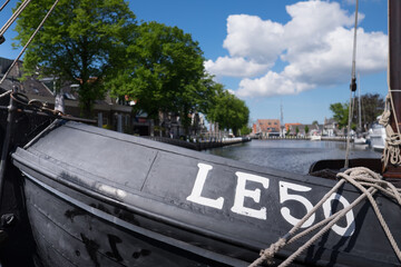 Canal with Lemsteraak LE50 in foreground, boats and houses mirrored in water in the center of  Lemmer near IJsselmeer in Friesland, Netherlands