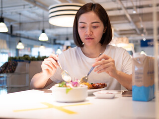Obraz na płótnie Canvas Asian woman sitting separated in restaurant eating food with table shield plastic partition to protect infection from coronavirus covid-19