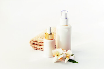 Fototapeta na wymiar Cosmetic tonic and serum unbranded white bottles, towel and jasmine blossom. Spa concept.