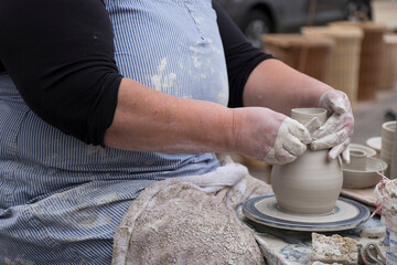 Hands of a woman working with clay on a rotating earthenware wheel and thus creating a vase