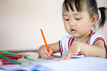 A young Asian female toddler with black hair is smiling. She happily with Colored pencils.And copy space.