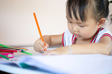 A young Asian female toddler with black hair is smiling.She happily with Colored pencils.And copy space.