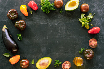 Frame of vegetables and herbs on chalkboard backdrop, healthy vegan food. Black background, top view, flat lay