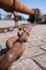 Big rusty chain used for fishing with boat lying in the harbor. Focus on the third ring
