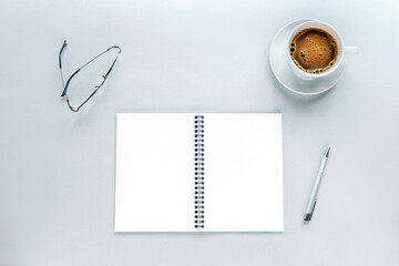 Cup of coffee and blank spiral notepad mockup on a grey background with pen and eyeglasses. Work from home concept. Top view, flat lay