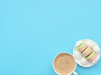 The cup of cappuccino and delicious macarons with white merengues on white plate  on blue background. Happy day, breakfast concepts. Greeting card. Flat lay style with copy space.