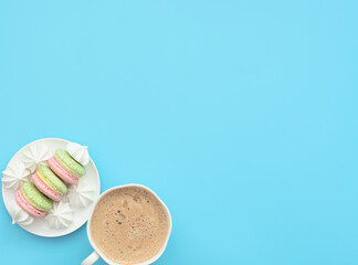 The cup of cappuccino and delicious macarons with white merengues on white plate  on blue background. Happy day, breakfast concepts. Greeting card. Flat lay style with copy space.