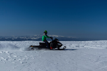 Fototapeta na wymiar Rider on the snowmobile in the mountains ski resort. A man is riding snowmobile in mountains