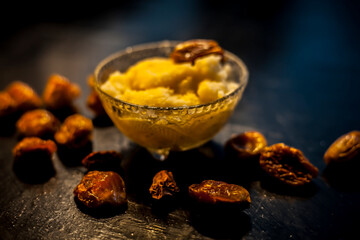 Close up shot of dates soaked in ghee for better stamina and health on black wooden surface along with ghee or clarified butter. Horizontal shot.