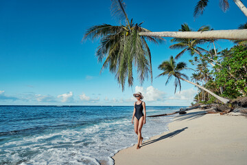 Fototapeta na wymiar Vacation on the seashore. Young woman walking away on the beautiful tropical white sand beach.