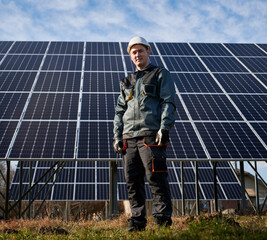 Man electrician in safety helmet standing near photovoltaic solar module. Male worker in gloves...