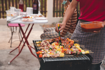 A man grilling pork and barbecue in dinner party. Food, people and family time concept.