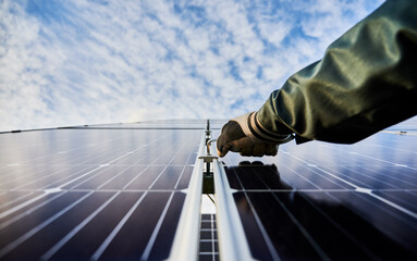 Close up of male worker hand in glove installing photovoltaic solar panel with beautiful cloudy sky...