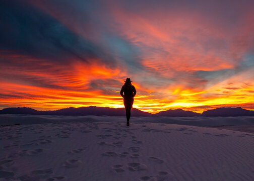 silhouette of a young woman in a cowboy hat reflecting on the sunset in White Sands National Park