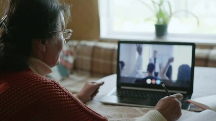 interactive training, attractive cheerful old woman undergoing training using video communication while sitting at a table at home during an online conference