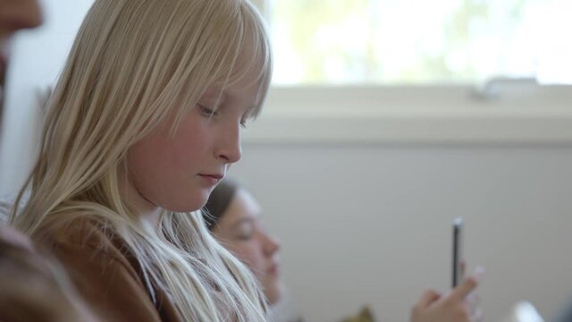 A young swedish girl looking at her phone while hanging out on a sofa with her cousins.