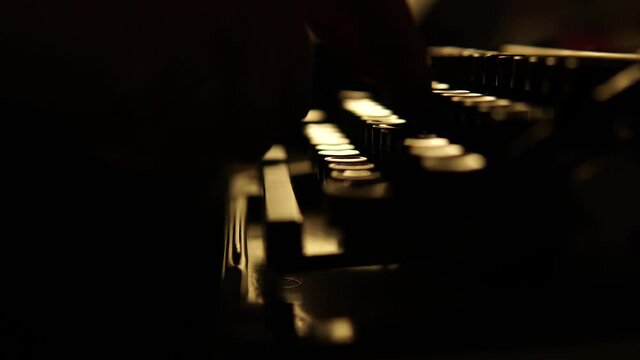 A man or woman works on a typewriter. Old typewriter on a dark background, close-up shot. Fingers press keys in dimly lit desk lamps. A dark room.