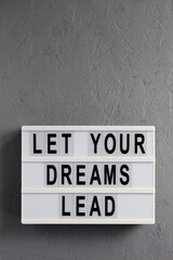 'Let your dreams lead' on a lightbox on a gray surface, top view. Flat lay, from above, overhead. Copy space.