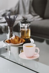 Herbal tea and fresh croissant served on a metal tray. Breakfast on a coffee table on living room