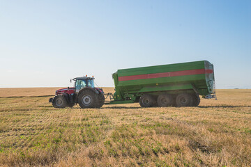 Obraz premium Grain harvest concept. Agricultural tractor with loader in mowed field on sunny day