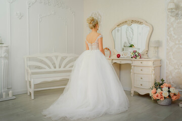 Gorgeous bride in a beautiful white wedding dress looks in the mirror on her wedding day