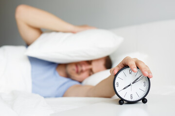 man waking up with alarm clock in bedroom at home